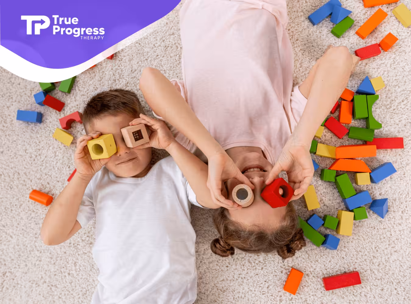 Two kids with autism laying on the floor playing with colorful blocks