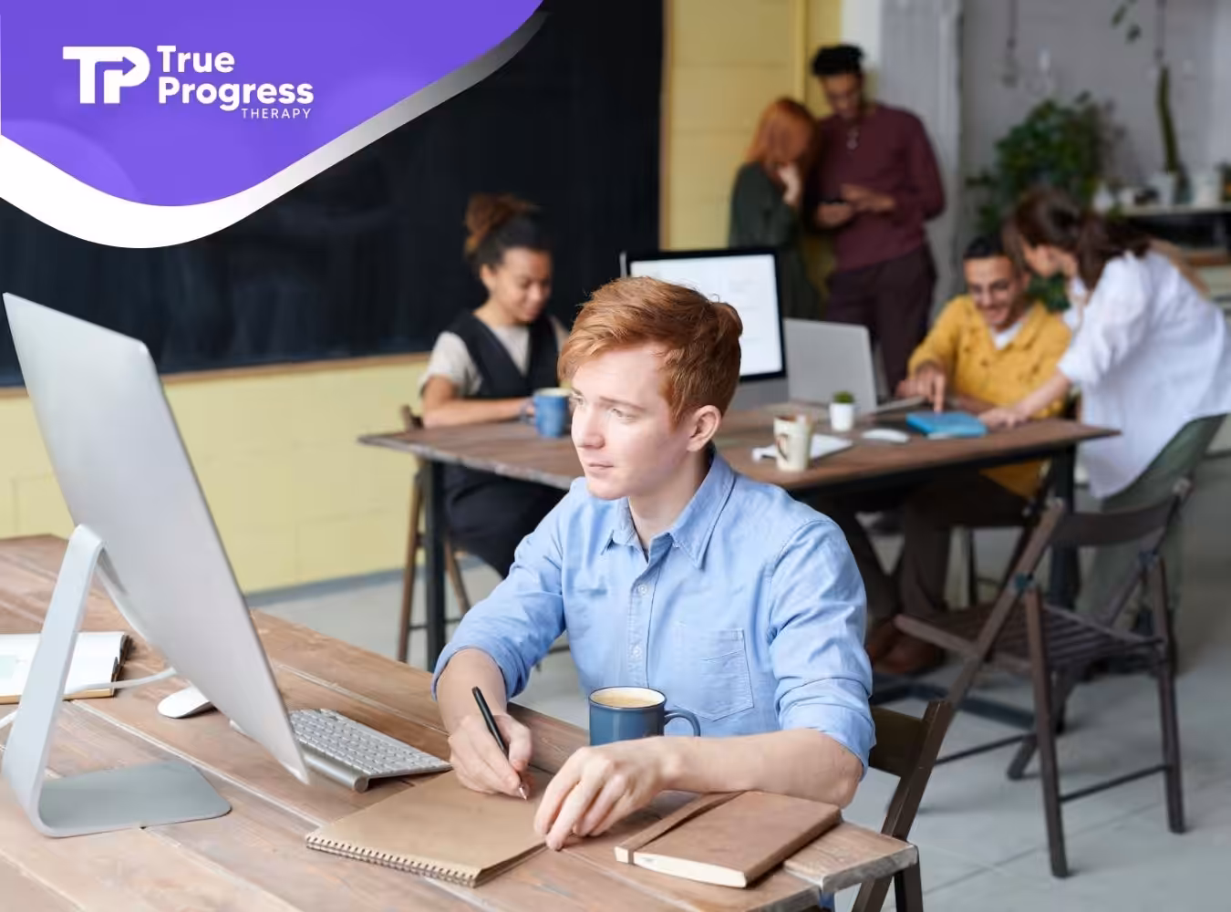 An autistic adult man focused on working at a computer desk in an office with coworkers in New Jersey.