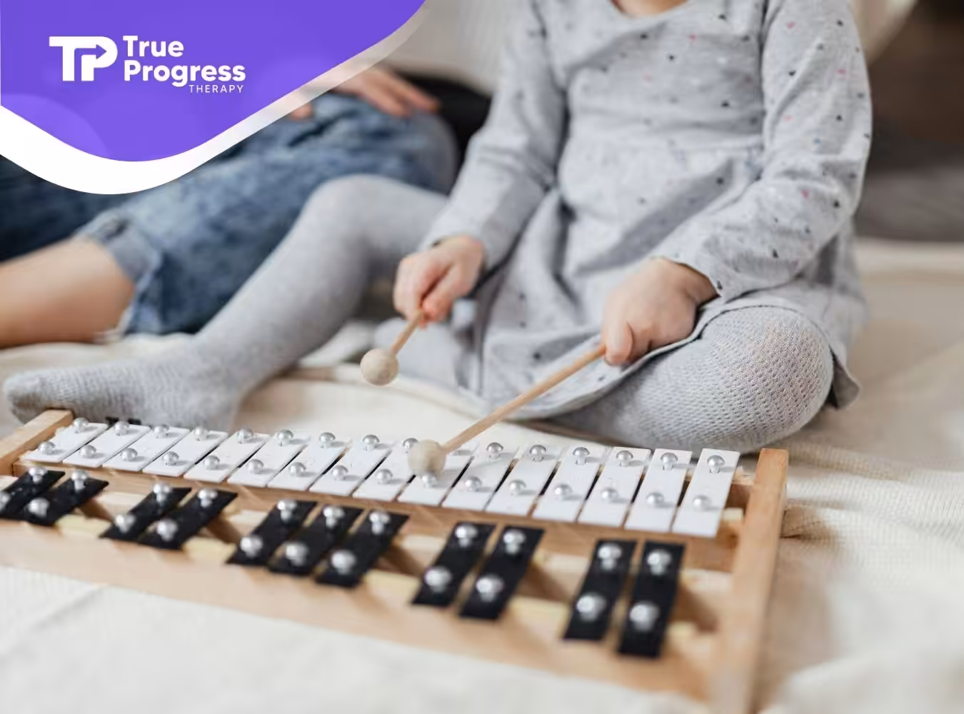 An autistic toddler playing a xylophone with mallets while sitting on a soft blanket in New Jersey.