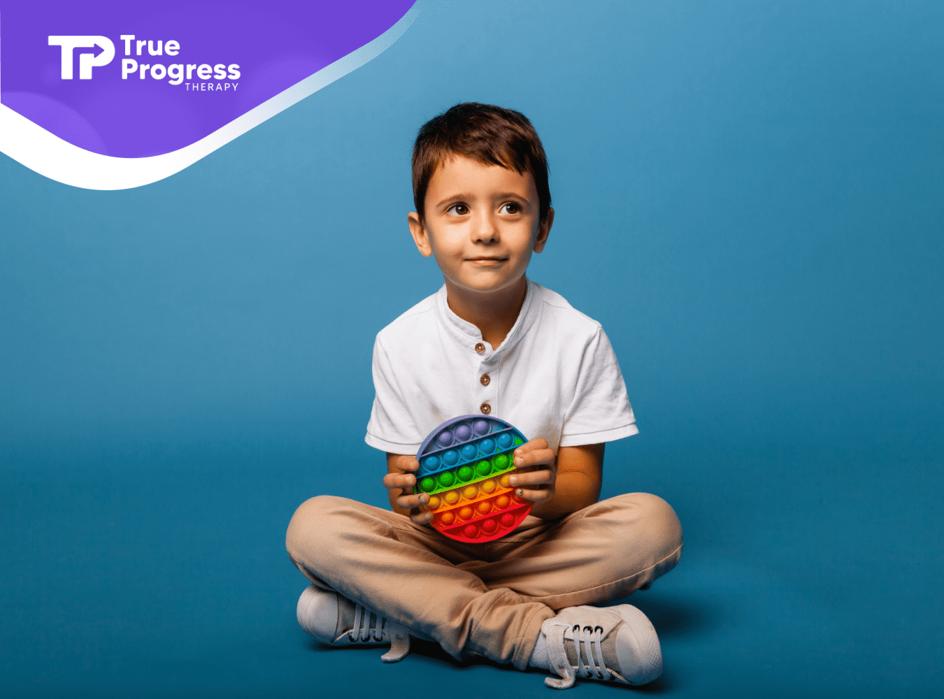 A child with autism is sitting on the floor holding a colorful fidget toy