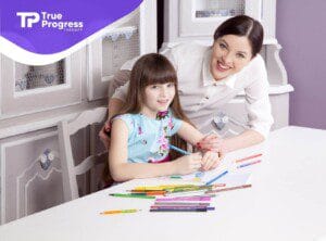 BCBA helping a girl draw at a table with colored pencils.