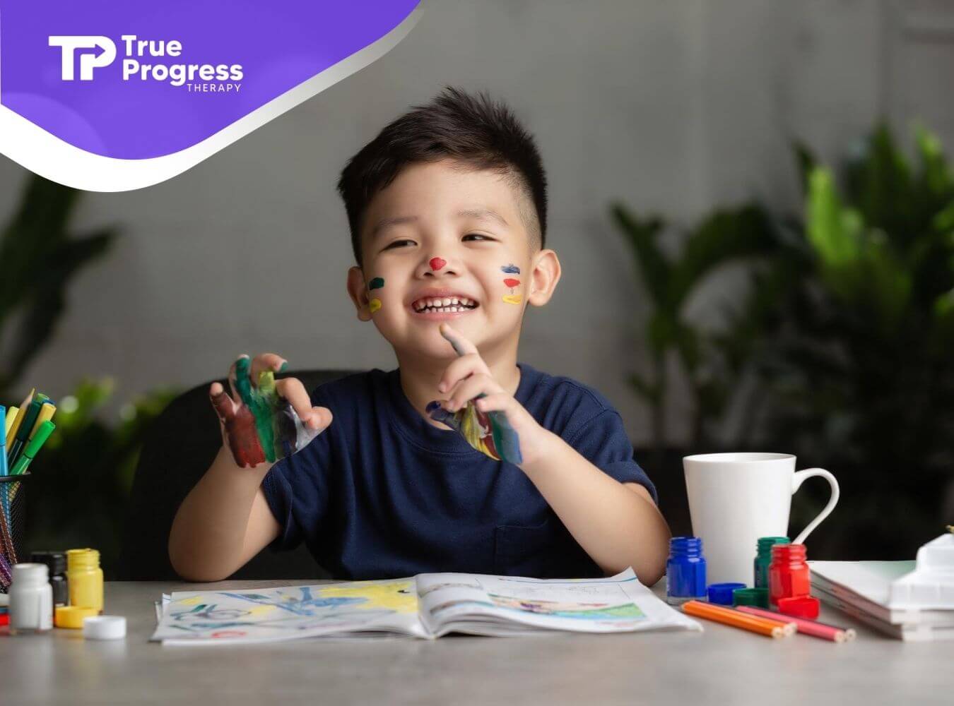 Smiling child with paint on their face and hands, painting at a table in ABA therapy.