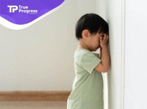 Toddler with autism standing with head against wall looking upset.