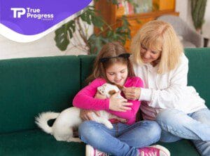 Child and BCBA smiling while cuddling a dog on a couch during ABA therapy.