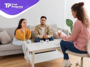 A young couple sits on a grey sofa for an ABA parent training session, speaking with a BCBA.