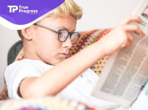 A young boy with blonde hair and glasses intently reading a newspaper in ABA therapy.