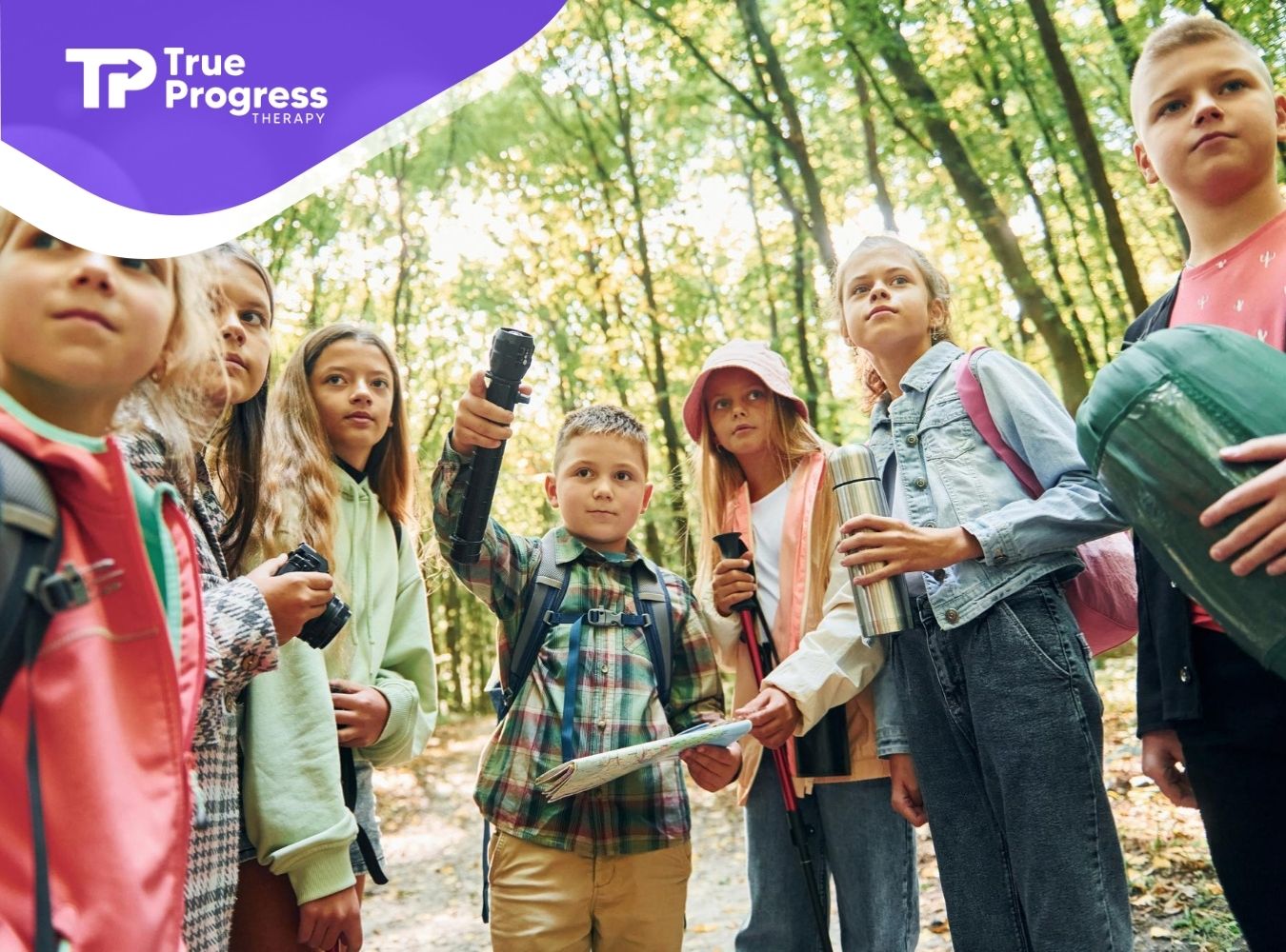Group of children with autism hiking in a forest, holding a map and outdoor gear.